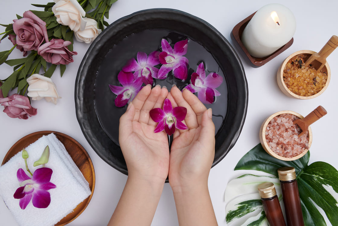 woman-soaking-her-hands-bowl-water-flowers-spa-treatment-product-female-feet-hand-spa-massage-pebble-perfumed-flowers-water-candles-relaxation-flat-lay-top-view (1) (1)